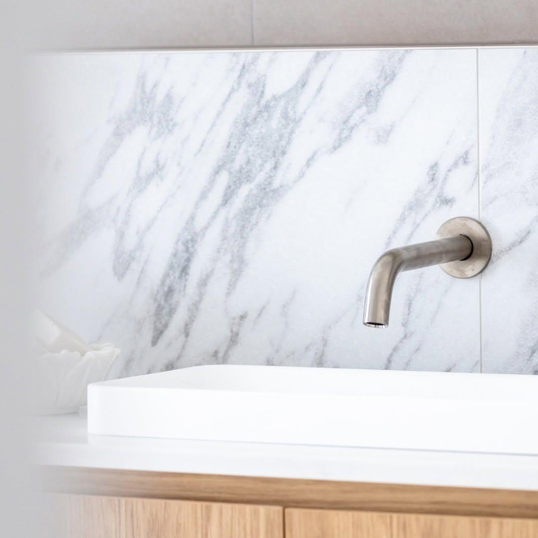 Wall-mounted tapware over a square basin against a marble tiled splashback