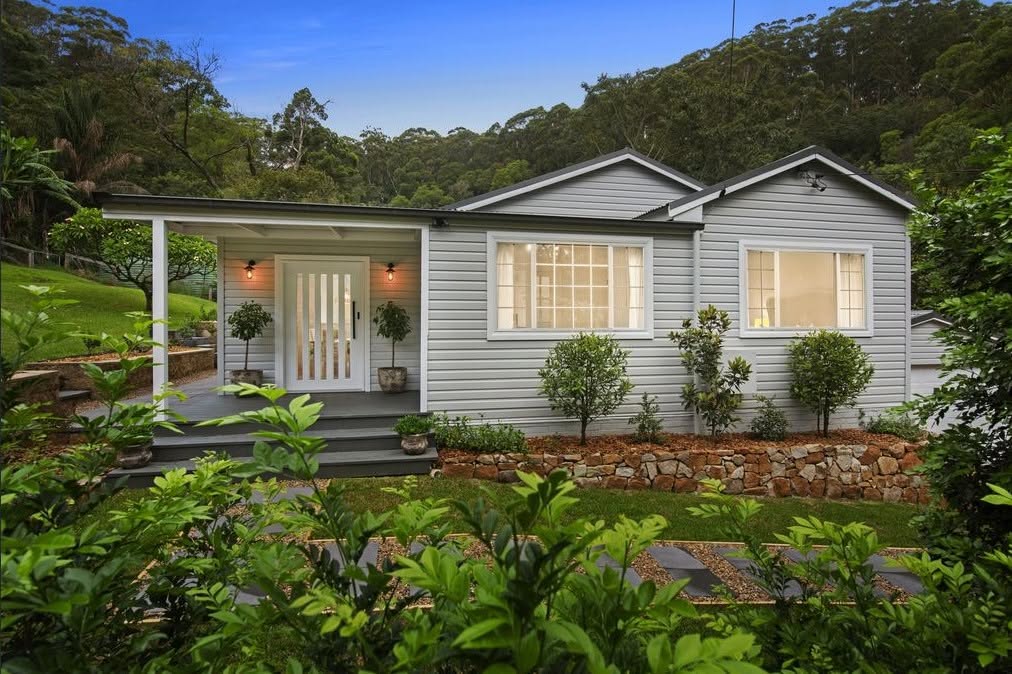 Renovated coastal cottage at dusk with warm lit windows and landscaped garden