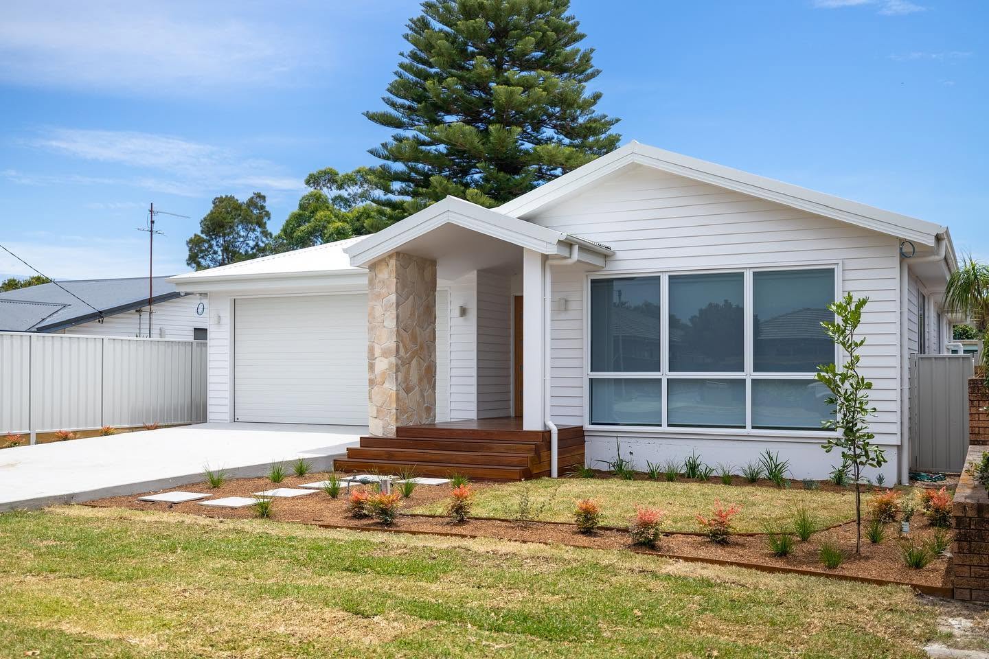 Single storey white weatherboard new build with stone entry pier and landscaped lawn