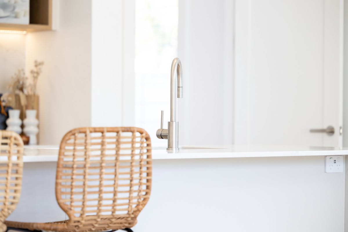 Kitchen island with stone benchtop, gooseneck mixer and rattan bar stools