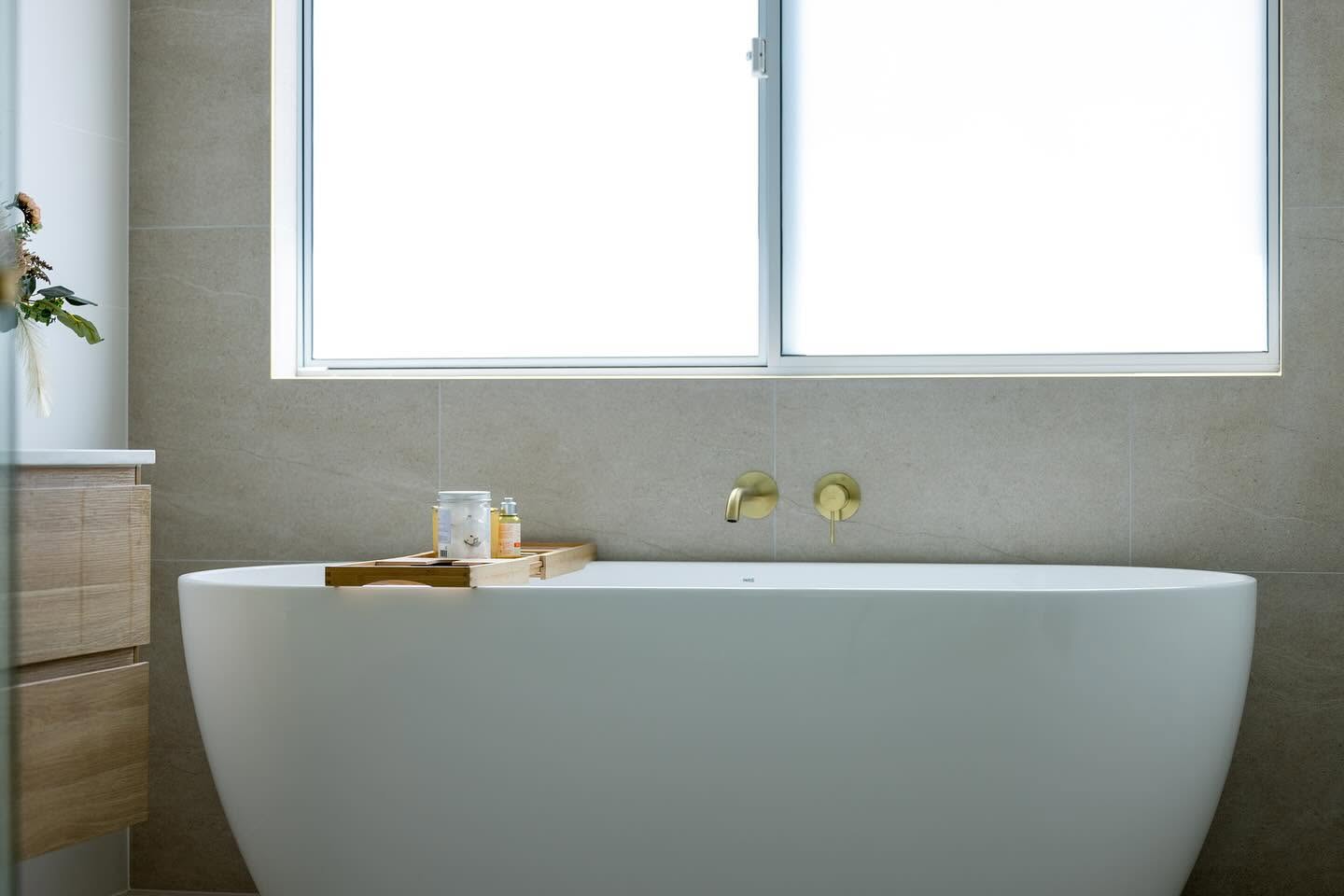 Freestanding bath below a window with brushed brass wall mounted tapware