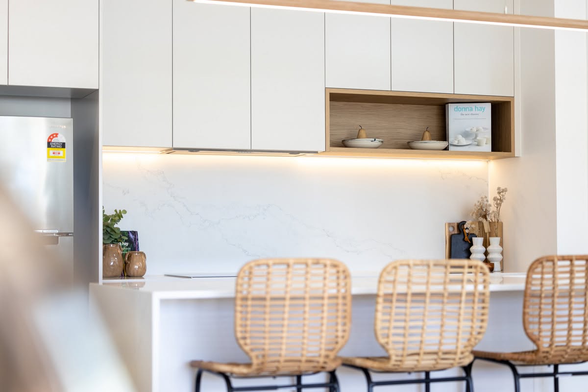 Handleless white kitchen with stone splashback, oak niche and rattan bar stools