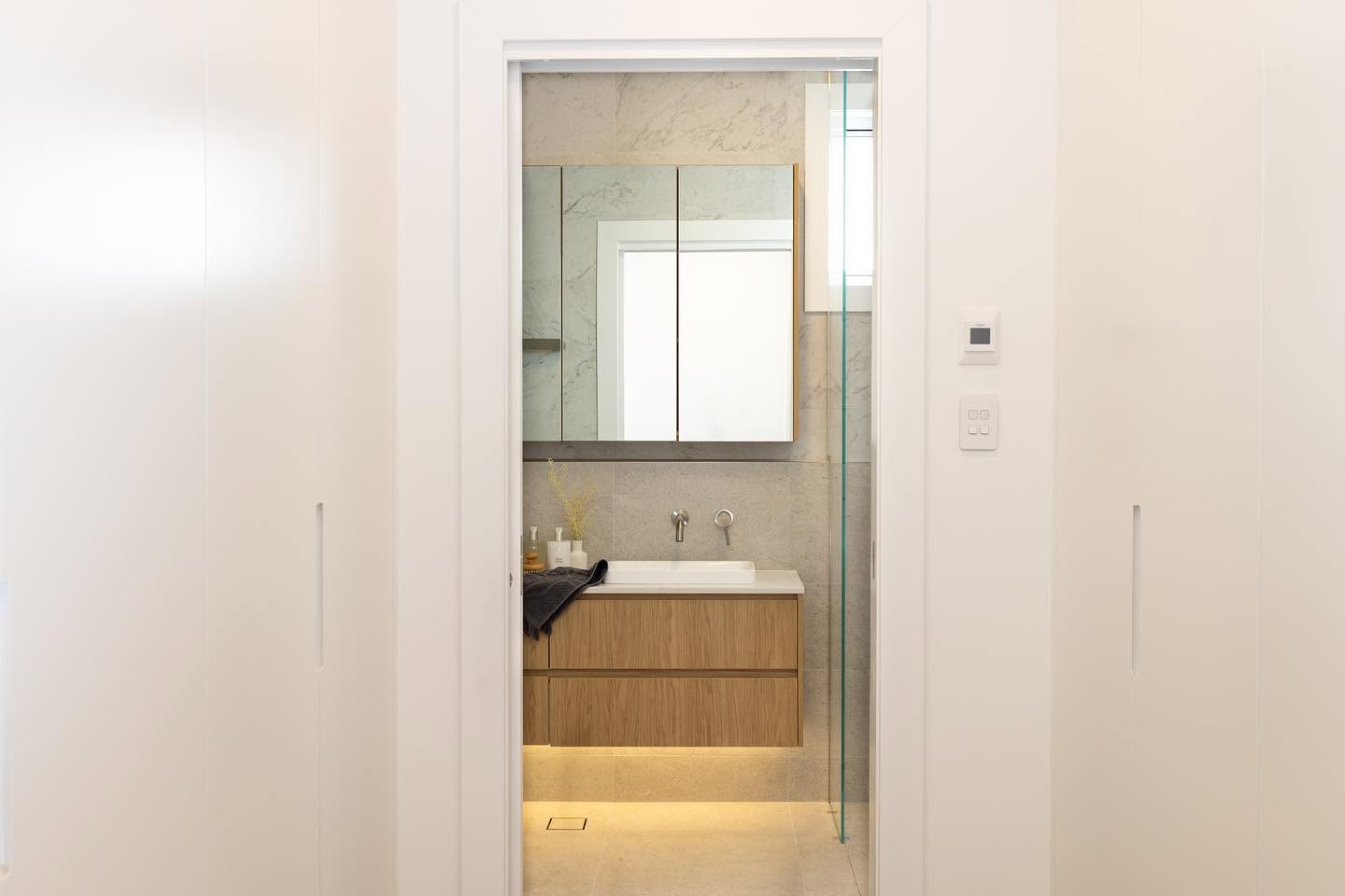 Ensuite viewed through a hallway with oak vanity, mirrored cabinet and under lighting