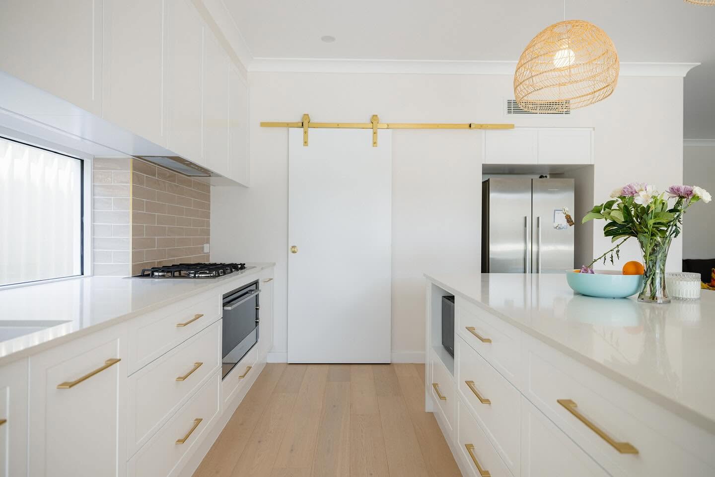White shaker kitchen with brass hardware, stone benchtops and a rattan pendant light
