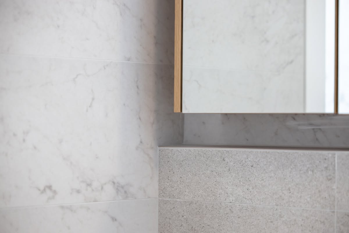 Detail of marble and stone bathroom tiling with an oak framed mirror