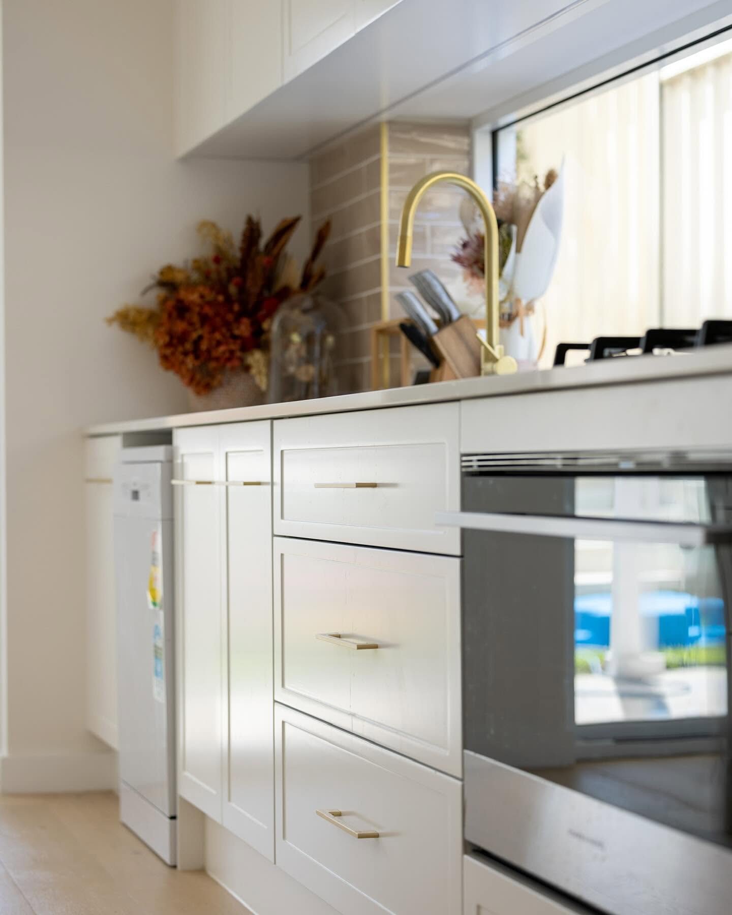 Shaker kitchen joinery with slim brass handles and a gooseneck brass mixer