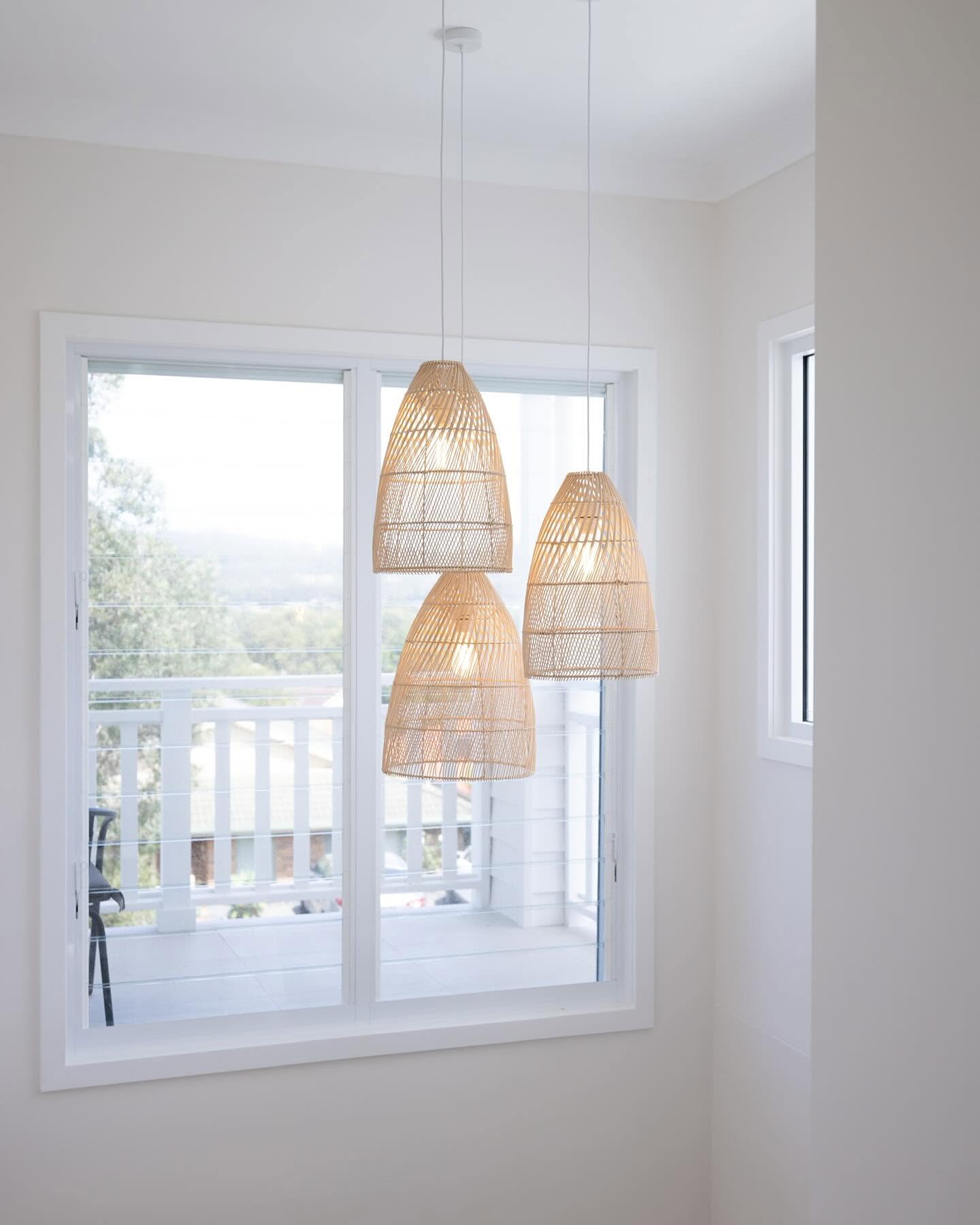 Rattan pendant lights beside a window with a leafy Central Coast outlook